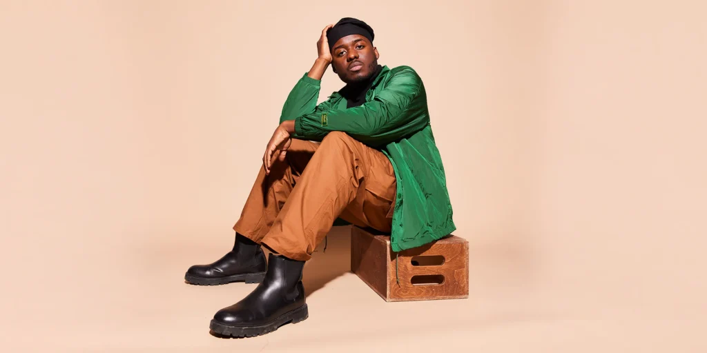 A man sits on a wooden box and stares at the camera.