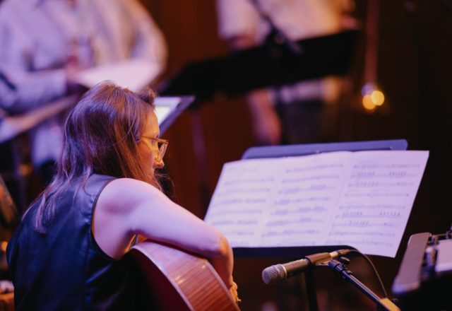 A musician plays a guitar while reading sheet music.
